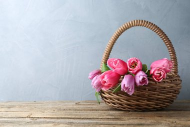 Hasır sepetteki güzel çiçekler ahşap masa üzerinde gri arkaplan, metin için alan