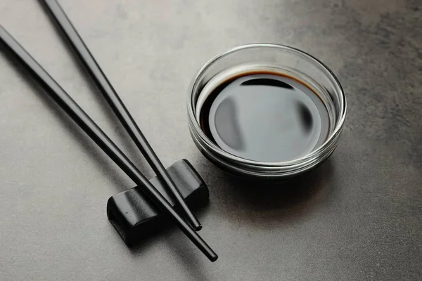Soya sosu cam kasede ve çubuklar gri masada, yakın plan.