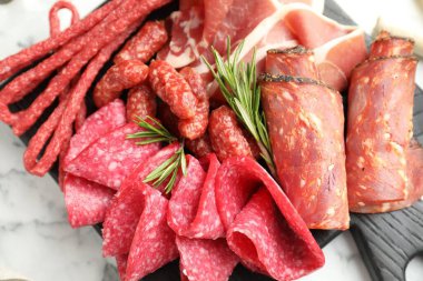 Beyaz mermer masa üzerinde farklı pişirilmiş et ve sosisler olan şarküteri tahtası.