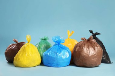 Açık mavi arka planda renkli poşetlerdeki çöpler. Metin için boşluk