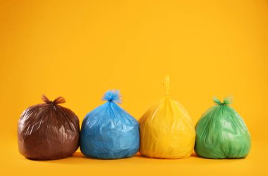 Sarı arka planda renkli poşetlerdeki çöpler. Metin için boşluk