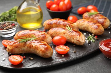 Lezzetli ızgara sosisler, domatesler, baharatlar, biberiye ve ketçap koyu dokulu masa, yakın plan.