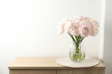 Güzel ranunculus çiçekleri cam vazoda beyaz duvarın yanındaki tahta çekmecelerin üzerinde. Metin için boşluk