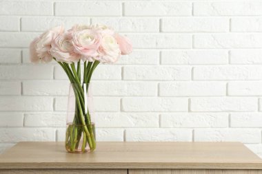Güzel ranunculus çiçekleri cam vazoda beyaz tuğla duvarın yanındaki tahta çekmece çekmecesinde. Metin için boşluk