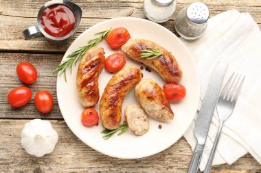 Ahşap masada servis edilen leziz ızgara sosisler, domatesler ve biberiye.