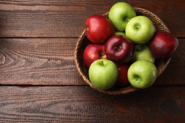 Hasır sepetteki yeşil ve kırmızı elmalar ahşap masanın üstünde, üst manzara. Metin için boşluk
