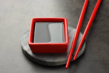 Soya sosu kasede ve çubuklar gri masada, yakın plan.