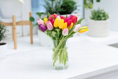 Beyaz masadaki vazoda renkli lalelerden oluşan güzel bir buket.