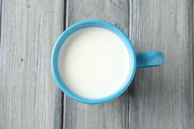 Gri ahşap masada kupada taze süt, üst manzara.