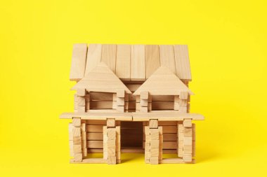 Sarı arka planda tahta bloklardan yapılmış ev