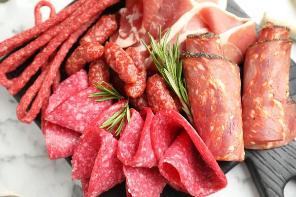Beyaz mermer masa üzerinde farklı pişirilmiş et ve sosisler olan şarküteri tahtası.