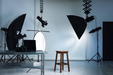 Profesyonel ışıklandırma ekipmanları fotoğraf stüdyosunda tavandan ve sandalyeden sarkıyor.