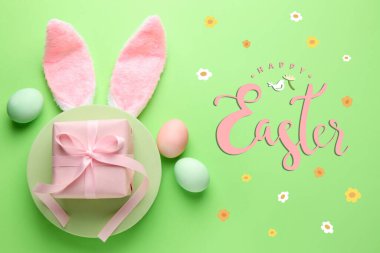 Mutlu Paskalya tebrik kartları ya da tavşan kulaklı posterler, açık yeşil arka planda boyanmış yumurtalar ve hediye kutuları, üst manzara