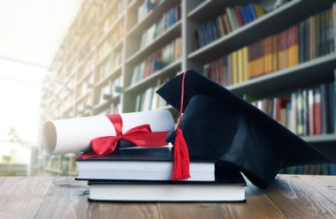 Diploma, mezuniyet şapkası ve kütüphanedeki ahşap masada kitaplar.