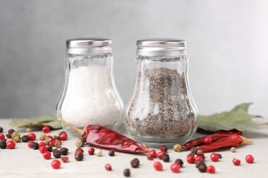 Açık gri masada baharatlı tuzluk ve biberlikler, yakın plan.