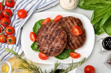 Lezzetli ızgara et köfteleri, domatesler ve beyaz fayanslı masada ıspanak.