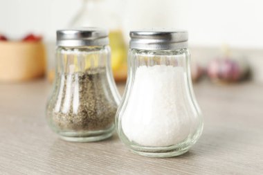 Beyaz duvarın yanındaki ahşap masada baharatlı tuzluk ve biberlikler.