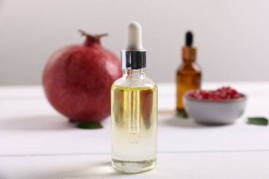 Beyaz ahşap masa üzerinde gerekli yağ ve taze nar şişeleri, yakın plan.