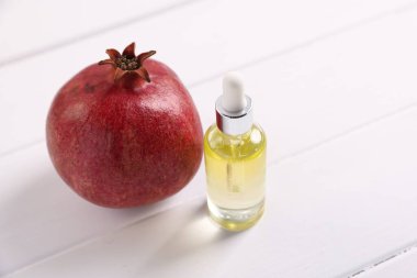 Bir şişe esaslı yağ ve beyaz ahşap masada taze nar, yakın plan.