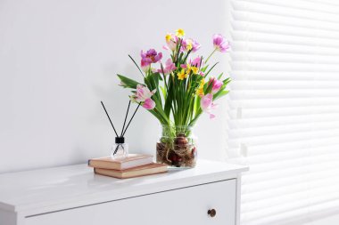 Vazoda güzel bahar çiçekleri, kitaplar ve sazlıklar pencerenin yanındaki şifoniyerde, metin için boşluk