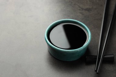 Soya sosu kasede ve çubuklar gri masada, yakın plan. Metin için boşluk