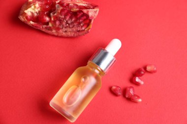 Gerekli yağ şişesi, taze nar parçası ve kırmızı arka planda tohumlar.