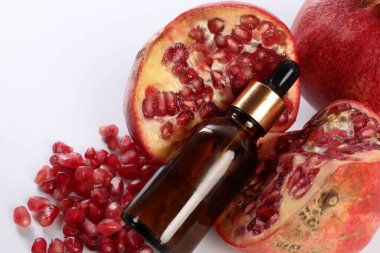 Bir şişe temel yağ ve beyaz zemin üzerinde taze nar.