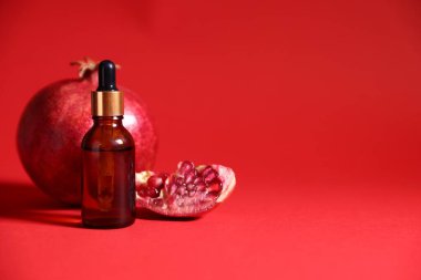 Kırmızı arka planda bir şişe gerekli yağ ve taze nar, yakın plan. Metin için boşluk