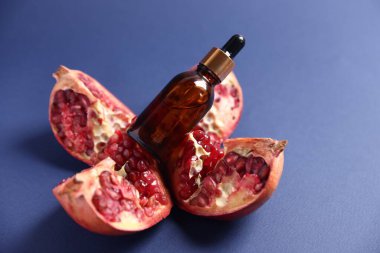 Bir şişe gerekli yağ ve mavi arka planda taze nar, yakın plan.