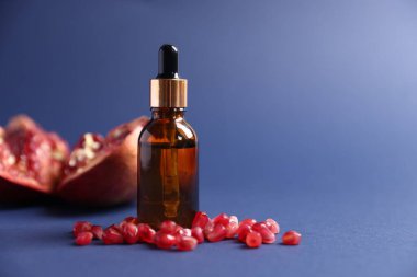 Bir şişe gerekli yağ ve mavi arka planda taze nar, yakın plan. Metin için boşluk