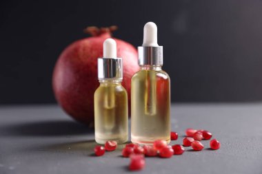 Gerekli yağ şişeleri ve gri arka planda taze nar, yakın plan.