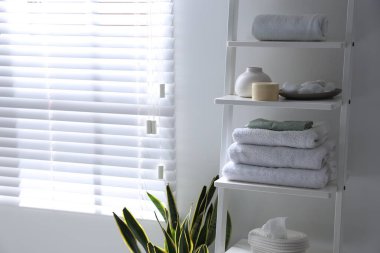Shelving unit with towels, vase, stones and cosmetic products indoors. Space for text