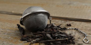 Tahta masanın üzerinde kuru çay yaprakları olan metal aşılayıcı, yakın plan.