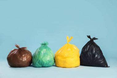 Açık mavi arka planda renkli poşetlerdeki çöpler. Metin için boşluk