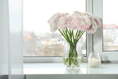 Cam vazoda güzel ranunculus çiçekleri ve beyaz pencere pervazında yanan mumlar. Metin için boşluk