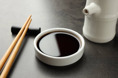 Soya sosu kasede ve çubuklar gri masada, yakın plan.