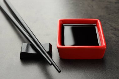 Soya sosu kasede ve çubuklar gri masada, yakın plan.