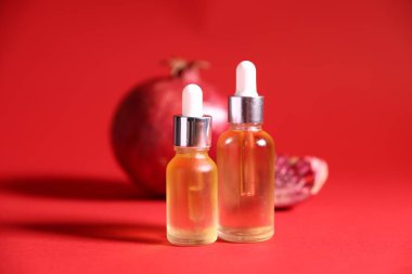 Kırmızı zemin üzerinde gerekli yağ ve taze nar şişeleri, yakın plan.