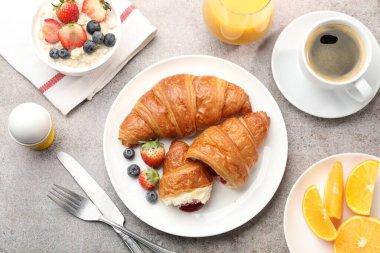 Nefis bir kahvaltı. Reçelli lezzetli kruvasanlar, böğürtlenler, içecekler ve açık gri masada yulaf ezmesi.