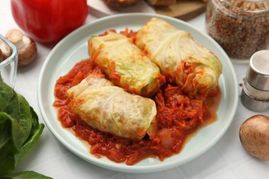 Lezzetli lahana dürümleri ve malzemeler beyaz döşemeli masada, yakın plan.