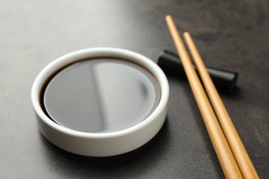 Soya sosu kasede ve çubuklar gri masada, yakın plan.