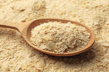 Arkaplan olarak kuru maya taneleri ve tahta kaşık yığını, yakın plan.