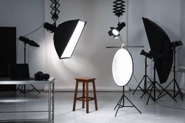 Profesyonel ışıklandırma ekipmanları fotoğraf stüdyosunda tavandan ve sandalyeden sarkıyor.