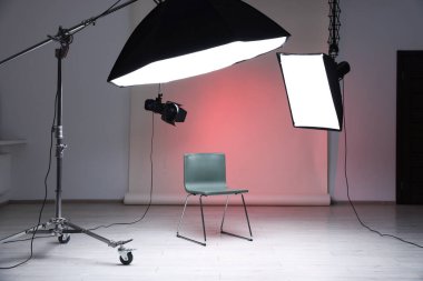 Profesyonel ışıklandırma ekipmanları fotoğraf stüdyosunda tavandan ve sandalyeden sarkıyor.