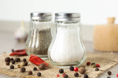 Beyaz duvarın yanındaki ahşap masada baharatlı tuzluk ve biberlikler.