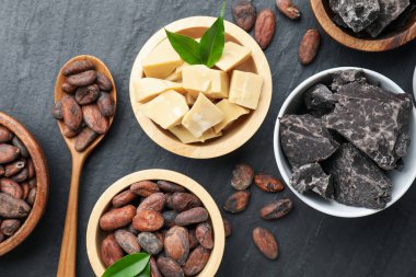 Organik kakao yağı, fasulye, çikolata parçaları ve yeşil yapraklar siyah masanın üzerinde, düz uzanmış