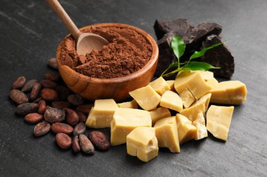 Organik kakao yağı, fasulye, çikolata parçaları, toz ve yeşil yapraklar siyah masada, yakın plan.