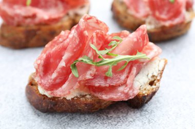 Salamlı, krem peynirli ve roka soslu leziz bruschetta açık gri desenli masa, yakın plan.