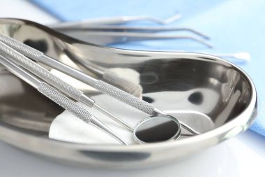 Böbrek çanağında farklı diş aletleri ve masada tıbbi peçete, yakın plan.