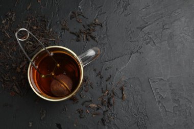Bir fincan çay, kuru yapraklar ve siyah masada metal infüzyon. Metin için boşluk